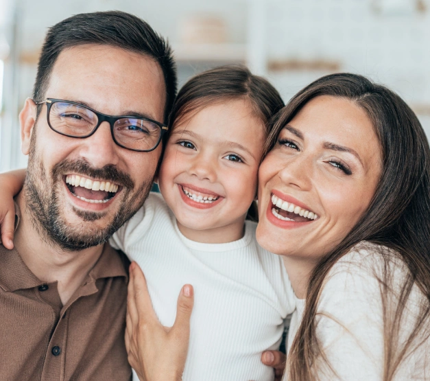 Happy family with young daughter smiling together indoors at dental office.
