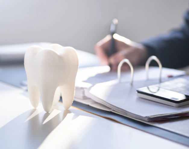 White tooth model on dental office desk with dentist writing in background