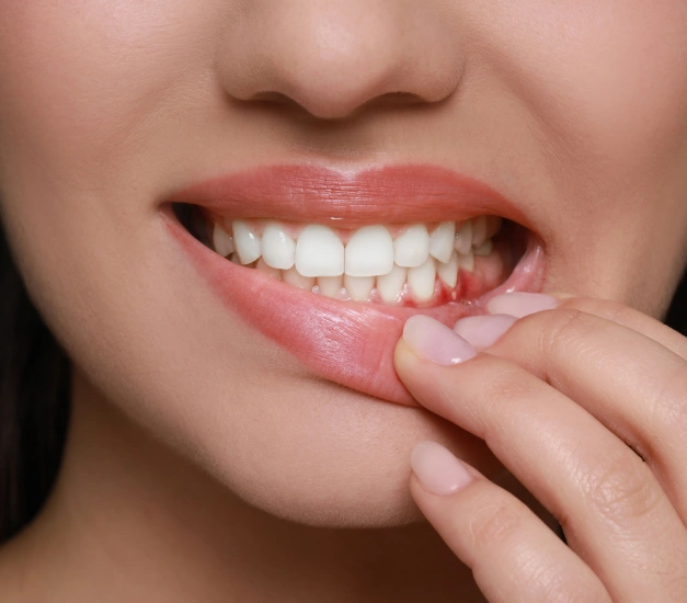 Woman displaying healthy white teeth while touching her lip with finger.