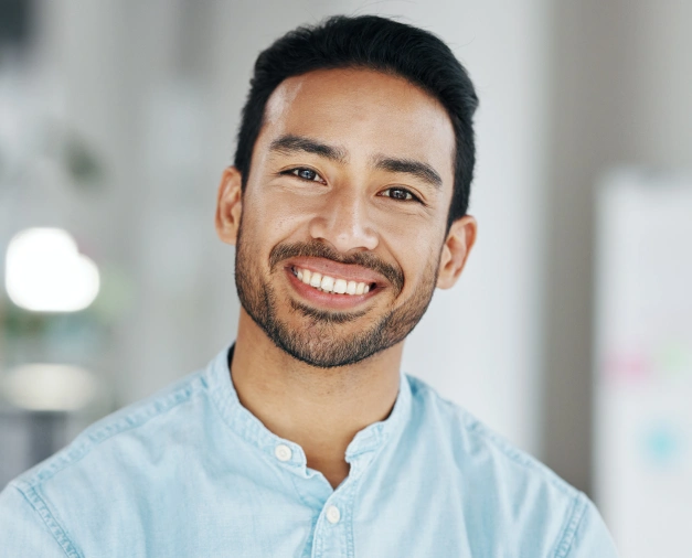Professional male dentist smiling at camera in bright clinical office setting.