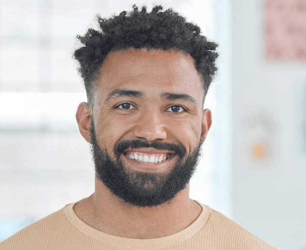 Smiling man in tan sweater against blurred office background at dental practice.