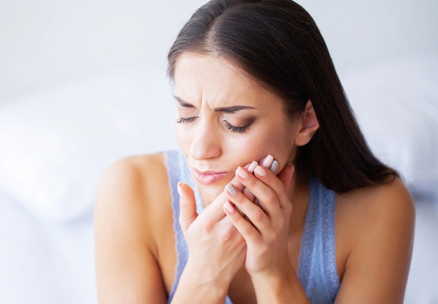 Woman holding cheek in pain, experiencing dental discomfort in indoor setting