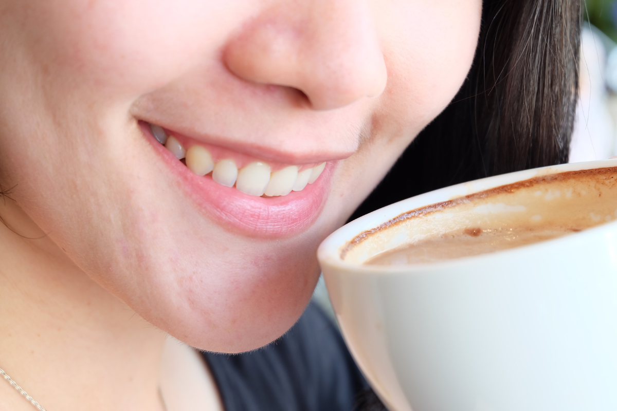 Woman with bright white teeth smiling while holding a coffee cup.