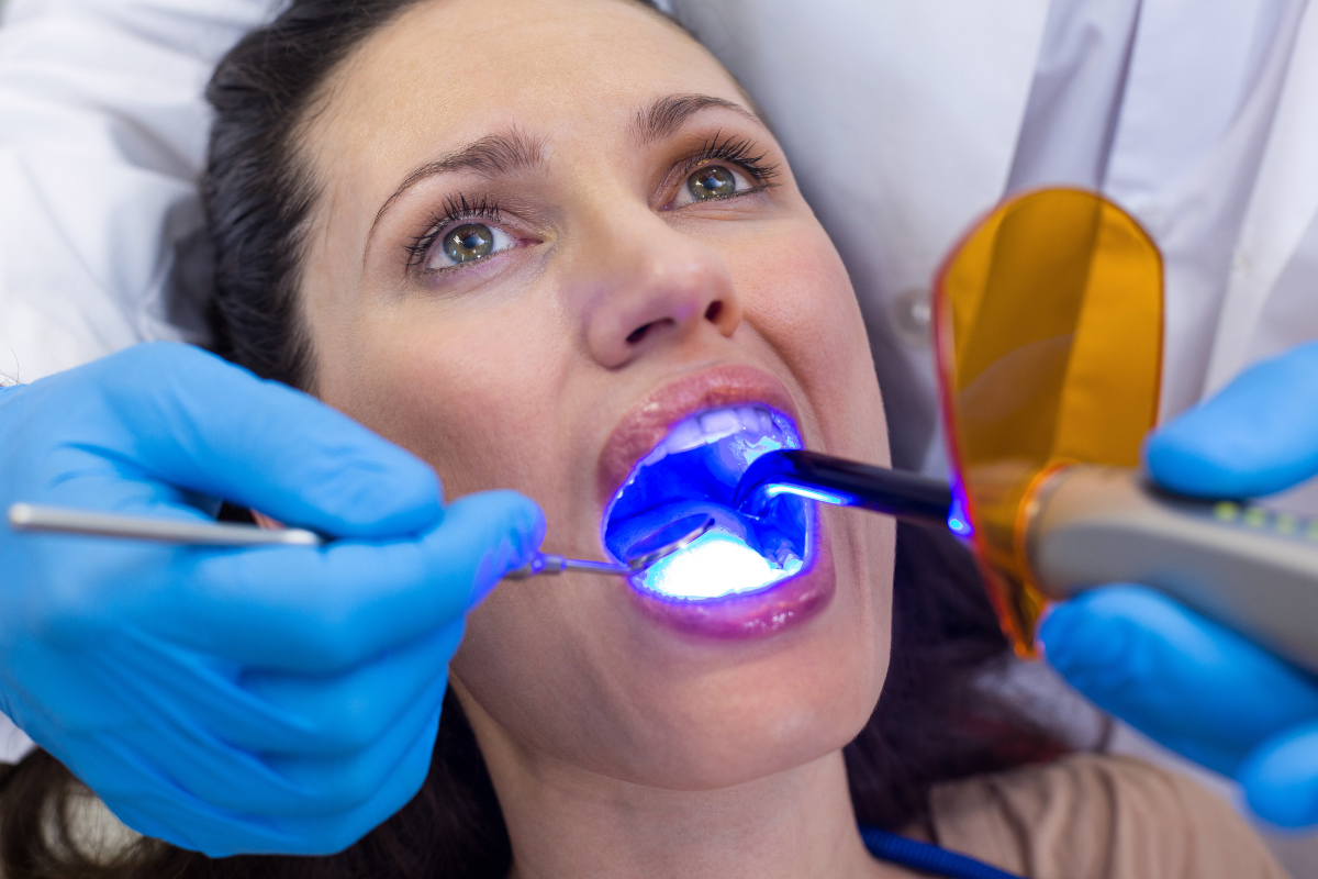 Dentist applying professional teeth whitening treatment with UV light to patient's teeth.